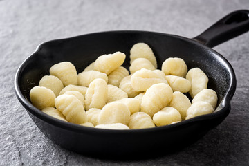 Raw gnocchi in cast iron frying pan on gray stone background.
