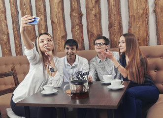Group of young people from two couples of guys and girls have a tea time in the cafe and making selfie by the smartphone with happiness