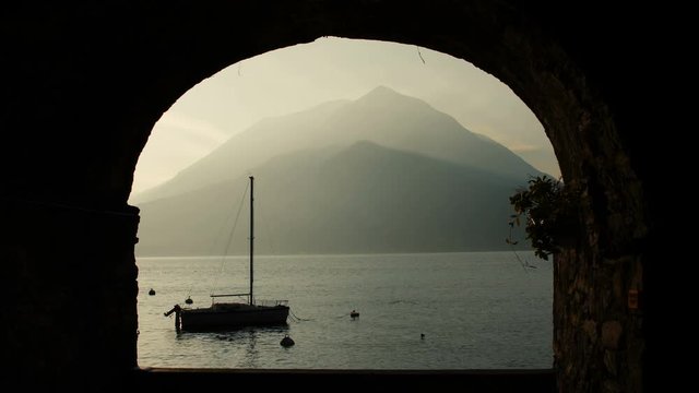 Boat on Lake Como at the sunset, mountain in the background, view through arch. Varenna, Lake Como, Italy.