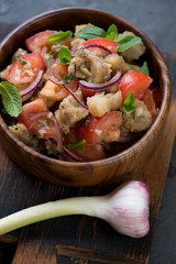 Closeup of a wooden bowl with baked aubergines and fresh tomatoes salad, selective focus