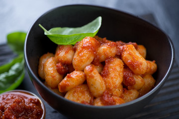 Close-up of potato gnocchi served with red pesto sauce and fresh basil in a black bowl