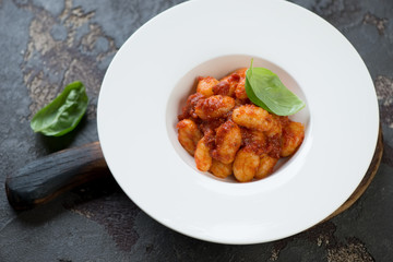 White glass plate with potato gnocchi with red pesto sauce on a dark brown stone background, studio shot