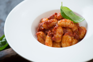 Close-up of potato gnocchi with red pesto sauce served in a white glass plate, selective focus