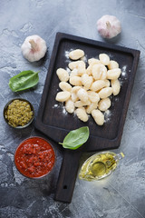 Black wooden serving board with uncooked potato gnocchi with red and green pesto, fresh green basil, garlic and olive oil, top view