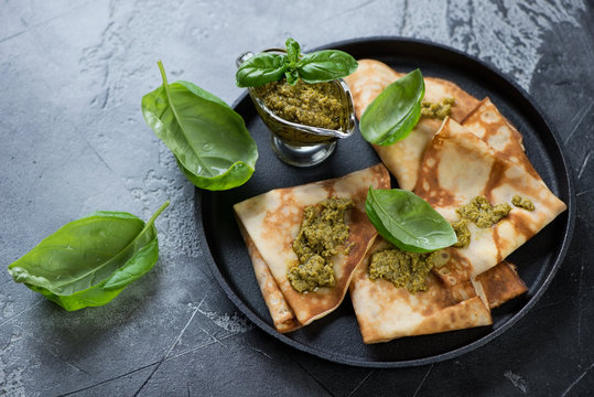 Frying pan with stuffed crepes topped with basil pesto sauce over grey stone background, studio shot