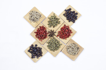 Several peppers, juniper and star anise on small wooden square bowls
