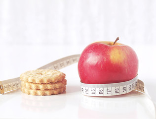Red apple and cookies with measuring tape on white background. Food choice