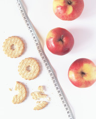 Red apples and cookies with measuring tape on white background. Food choice. Flat lay. Top view