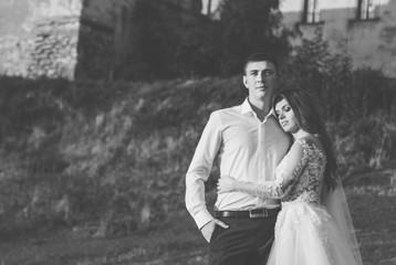 Beautiful bride leans to groom's chest standing near castle. Black and white feeling photo, happy wedding day