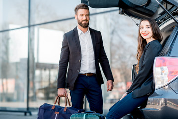 Business couple sitting in the car trunk with suitcase in the city. Business traveling by car concept