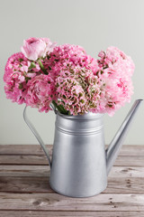 pink persian buttercup flowers. Curly peony ranunculus in Metallic gray vintage watering can, copy space.
