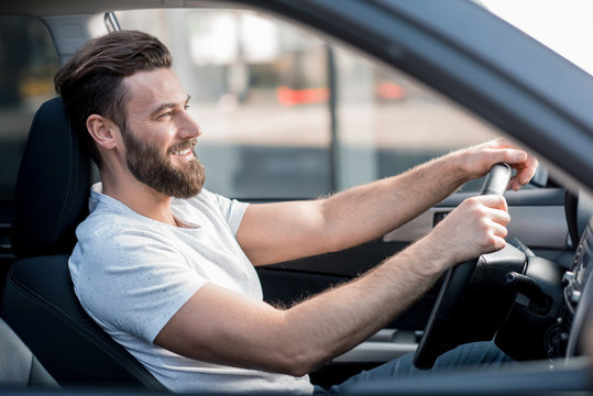 Handsome smiling man dressed casual in white t-shirt driving a car in the city