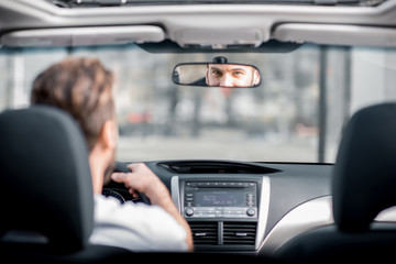 Man in white t-shirt driving a car in the city. Back view with the reflection on the mirror