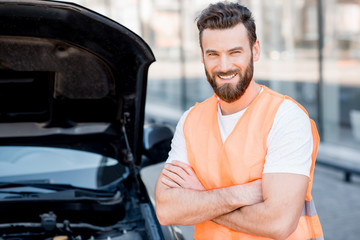 Portrait of a handsome worker of an technical assistance service standing near the car