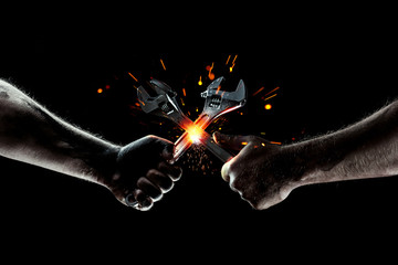 The battle of mechanics. Two wrenches cut sparks. Strong man's hands with wrenches
