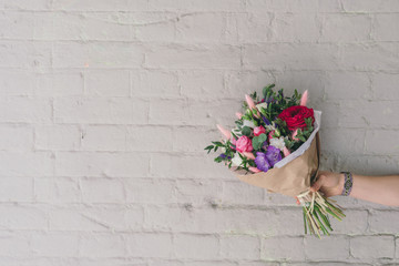Fototapeta na wymiar Stylish bouquet of fresh flowers against brick wall. Composition from freesia, roses, eucalyptus leaves in hand with free space for text