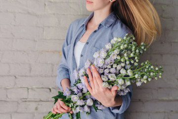 Young woman holds a bunch of delphinium flowers against an old brick wall. Beautiful spring floral background