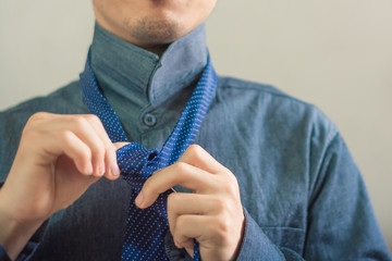 Asian guy trying to tight his necktie on with copy space