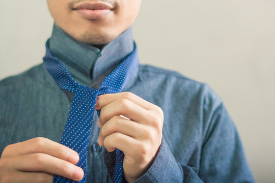 Asian guy trying to tight his necktie on with copy space
