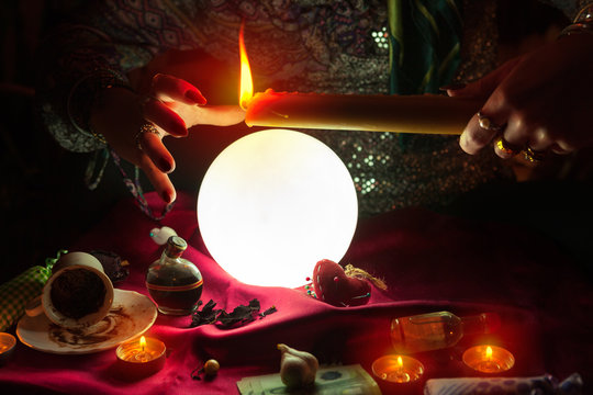 Candle in hand of fortune teller woman above crystal ball