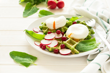 Healthy breakfast: spinach waffles with radish slices and poached eggs on white wooden table. Selective focus