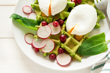 Healthy breakfast: spinach waffles with radish slices and poached eggs on white wooden table. Selective focus