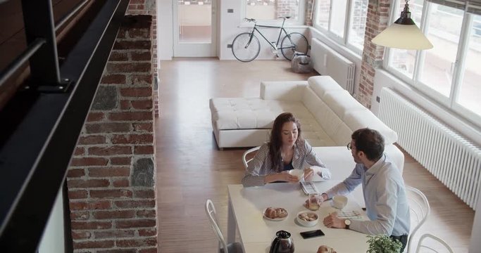 young caucasian couple in love having italian breakfast indoor in modern industrial house. smartphone use. 4k handheld top view overhead video shot