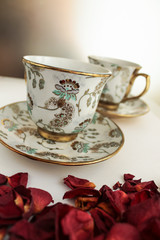 Tea cup and saucer on white table with rose petals