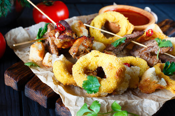 Grilled meats assortment, onion rings in breadcrumbs, rusks decorated with chili peppers, herbs and spices