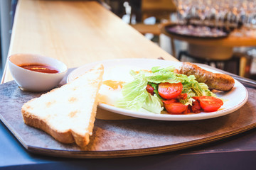 Fried eggs with appetizing sausages, toast bread and fresh salad.