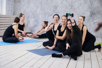 Making selfie. Group of girls in fitness class at the break looking at cell phone, happy and smiling, show funny face. Woman friendship, healthy modern life of young people concept.