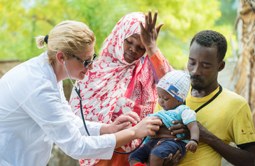 Female Caucasian doctor listening breath and heart beat of little African baby with stethoscope.Father holding the baby, mother looking down