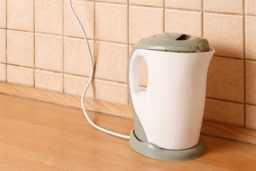 Electric kettle on wooden table in front of tiled wall angle view