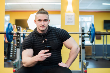 Fototapeta na wymiar Young handsome man using phone while having exercise break in gym.