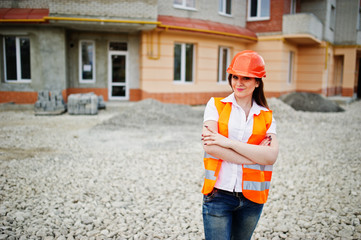 Engineer builder woman in uniform waistcoat and orange protective helmet against new building....