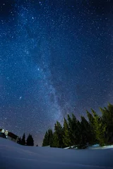 Foto op Plexiglas Prachtig landschap van een nachtelijke wintersterrenhemel boven dennenbos, lange belichtingsfoto van middernachtsterren en besneeuwd boslandschap © artiemedvedev