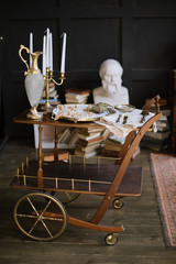 A vintage trolley on wheels with a candlestick, a golden jug and a tray with ornaments on it