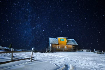 Foto auf Acrylglas Beautifull scenery of a night winter starry sky wooden house, long exposure photo of midnight stars and snowy yard near small village cabin in countryside © artiemedvedev
