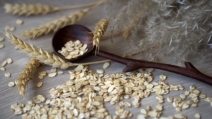 Close-up unprocessed Oat flakes with wooden spoon and different Ears against a plain coarse linen...