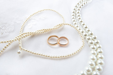 Fototapeta na wymiar Gold wedding rings lie on a wedding dress. Against the background of the necklace of pearls 