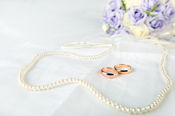 Gold wedding rings lie on a wedding dress. Against the background of the necklace of pearls 