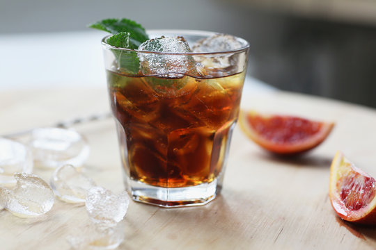 Cocktail whiskey cola with ice in a glass. On a wooden board are fragments of fruit. Photo with depth of field.