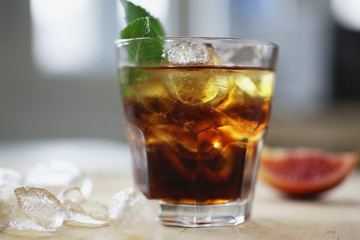 Cocktail whiskey cola with ice in a glass. On a wooden board are fragments of fruit. Photo with depth of field.