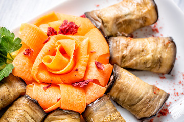 Eggplant rolls with cheese and carrots like rose on white plate with selective focus and top view