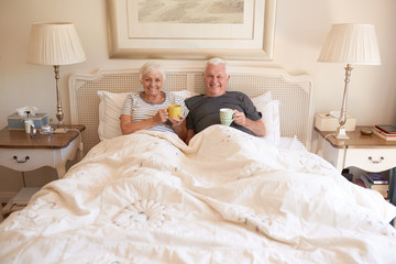 Content senior couple sitting in bed together drinking coffee