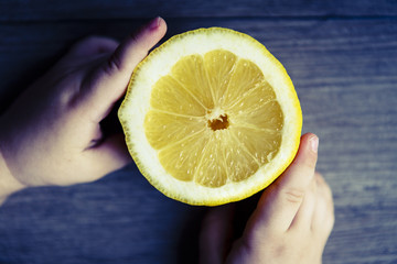 beautiful fresh yellow lemon in child hands on the wooden rustic table