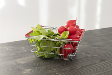 Bunch of fresh red radish in a basket on a wooden background