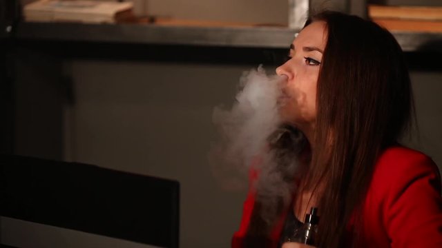 Close-up brunette in a red jacket, works with his laptop and smokes an electronic cigarette in a public place