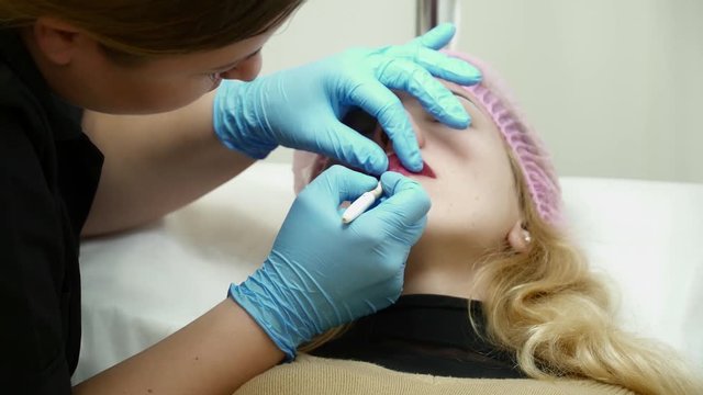 Beautician preparing woman for the permanent makeup of lips in salon