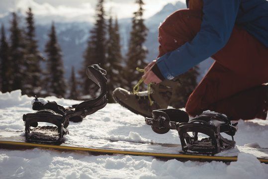 Low section of woman wearing shoe by snowboard at mountain